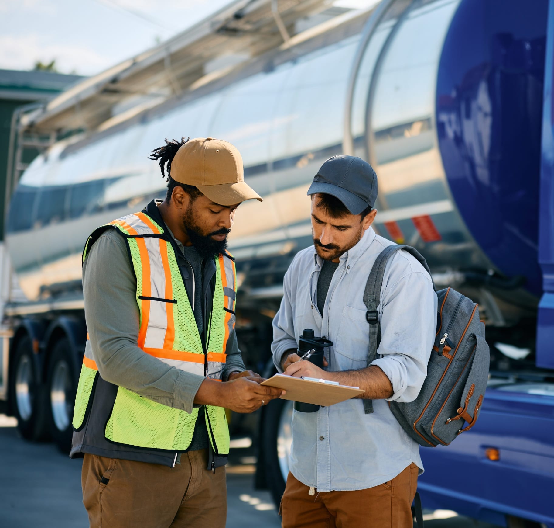 Brightline dispatcher and driver reviewing paperwork in front of a stainless tanker truck