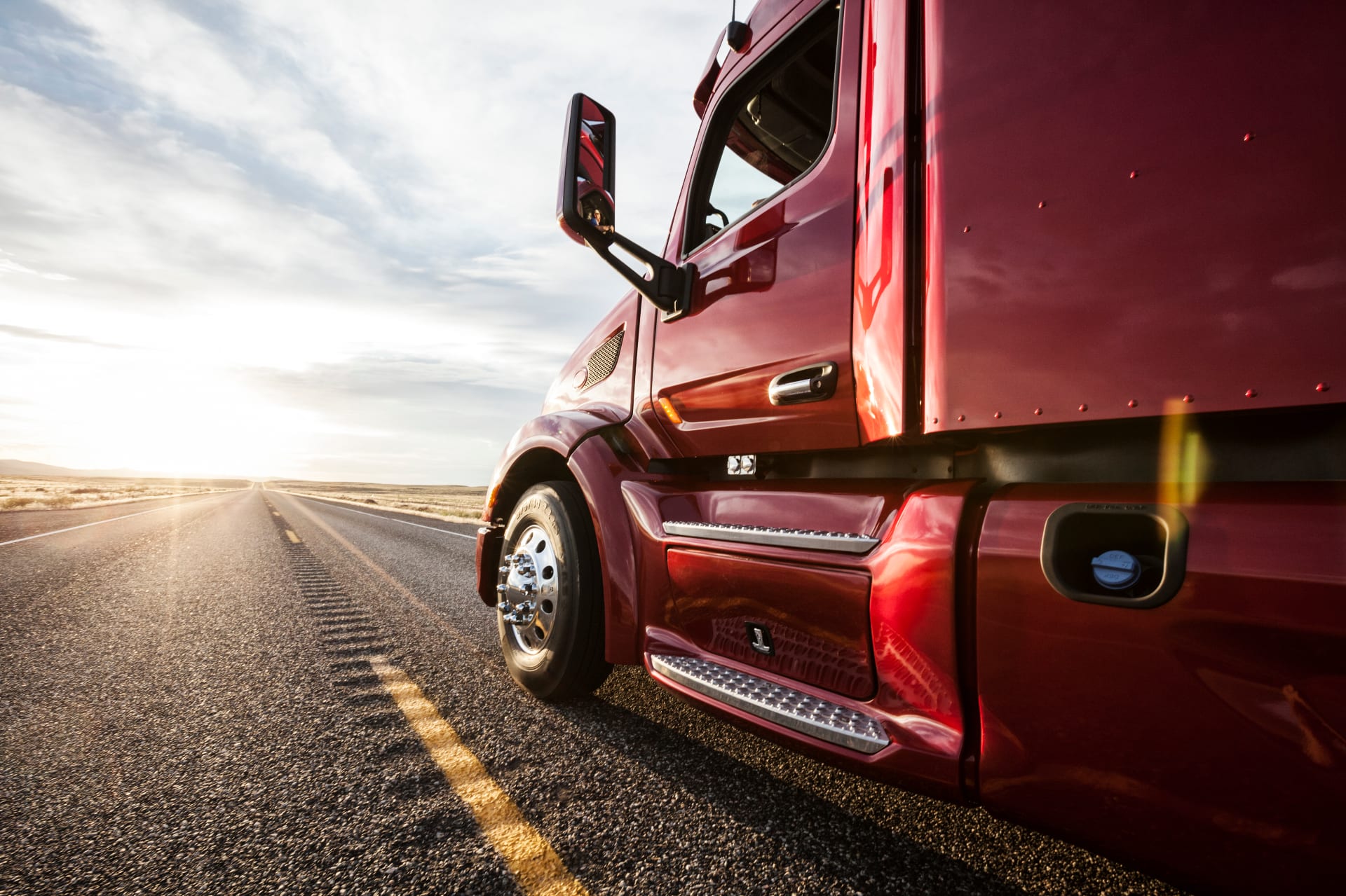 Close-up side view of a red commercial truck driving down a highway at sunset